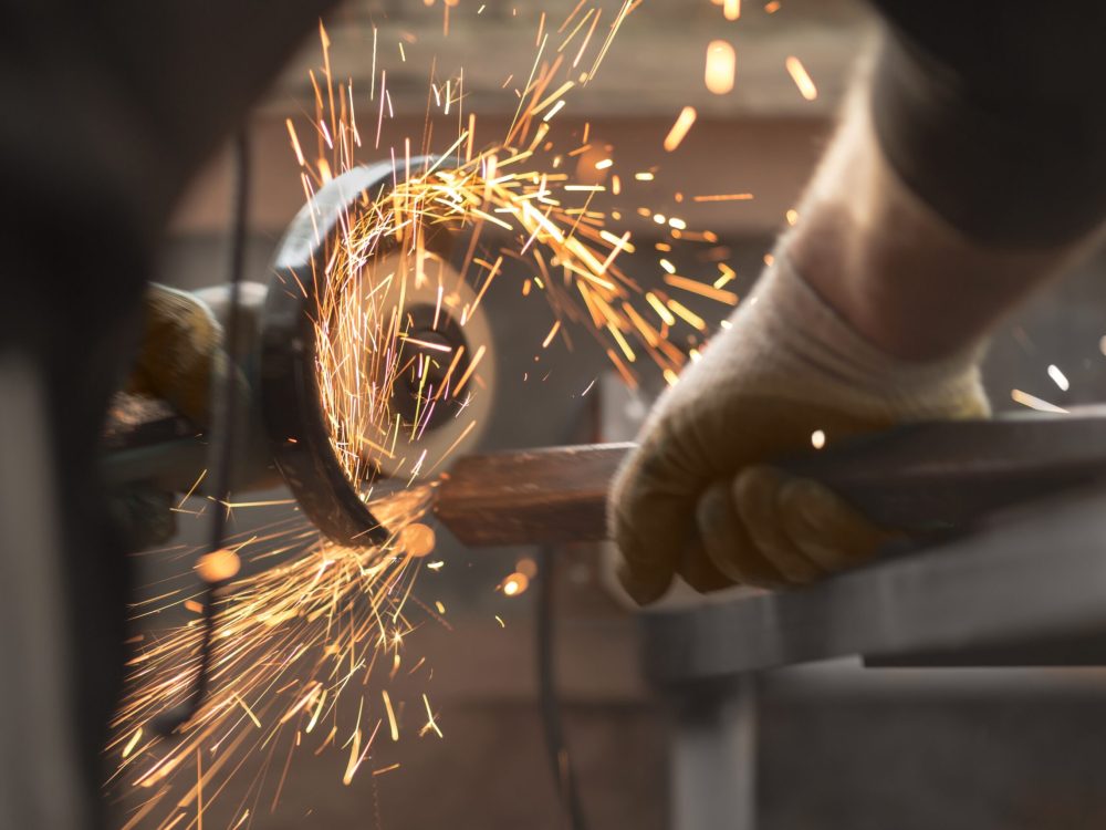 bulgarian angle grinder rotates the disc, a person cuts off the metal profile with his hands, sparks fly, beautiful glow, bokeh, orange light on a black background, production, flash of light