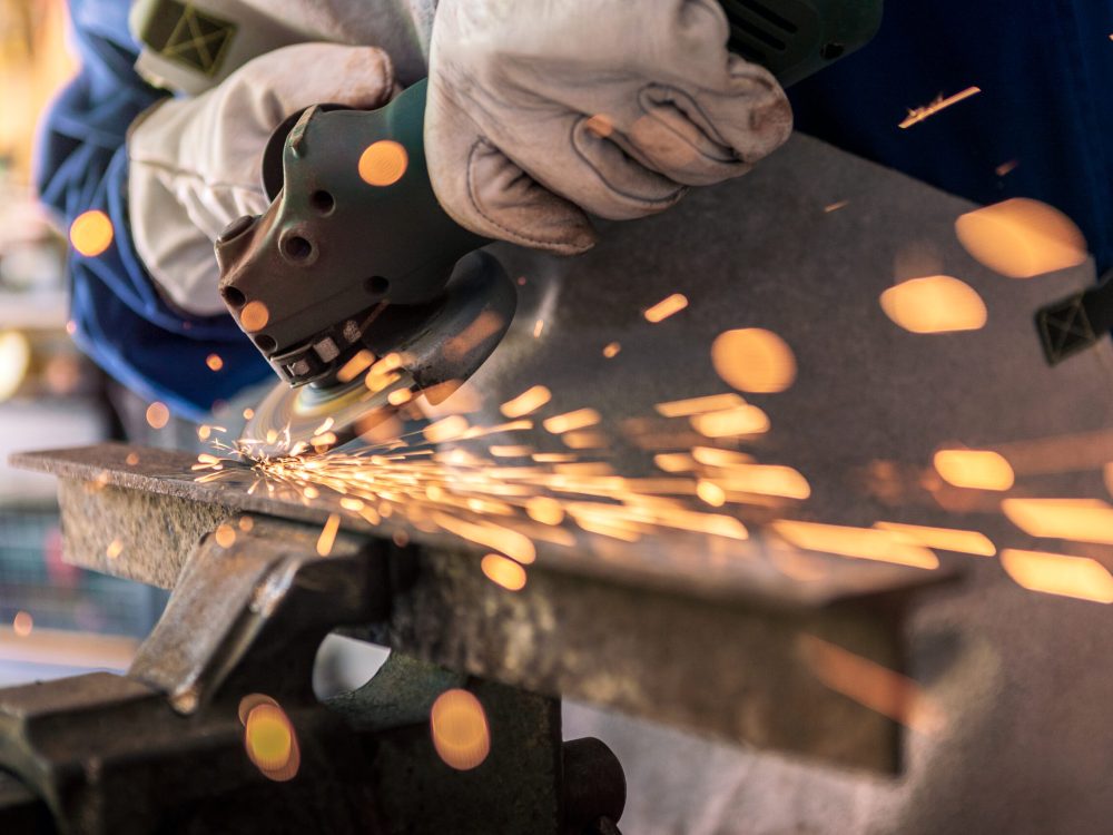 Worker grinding metal with a grinder and cleaning the steel seam. Working in a metal processing workshop. The man works with an electric tool. Sparks from metal heating.